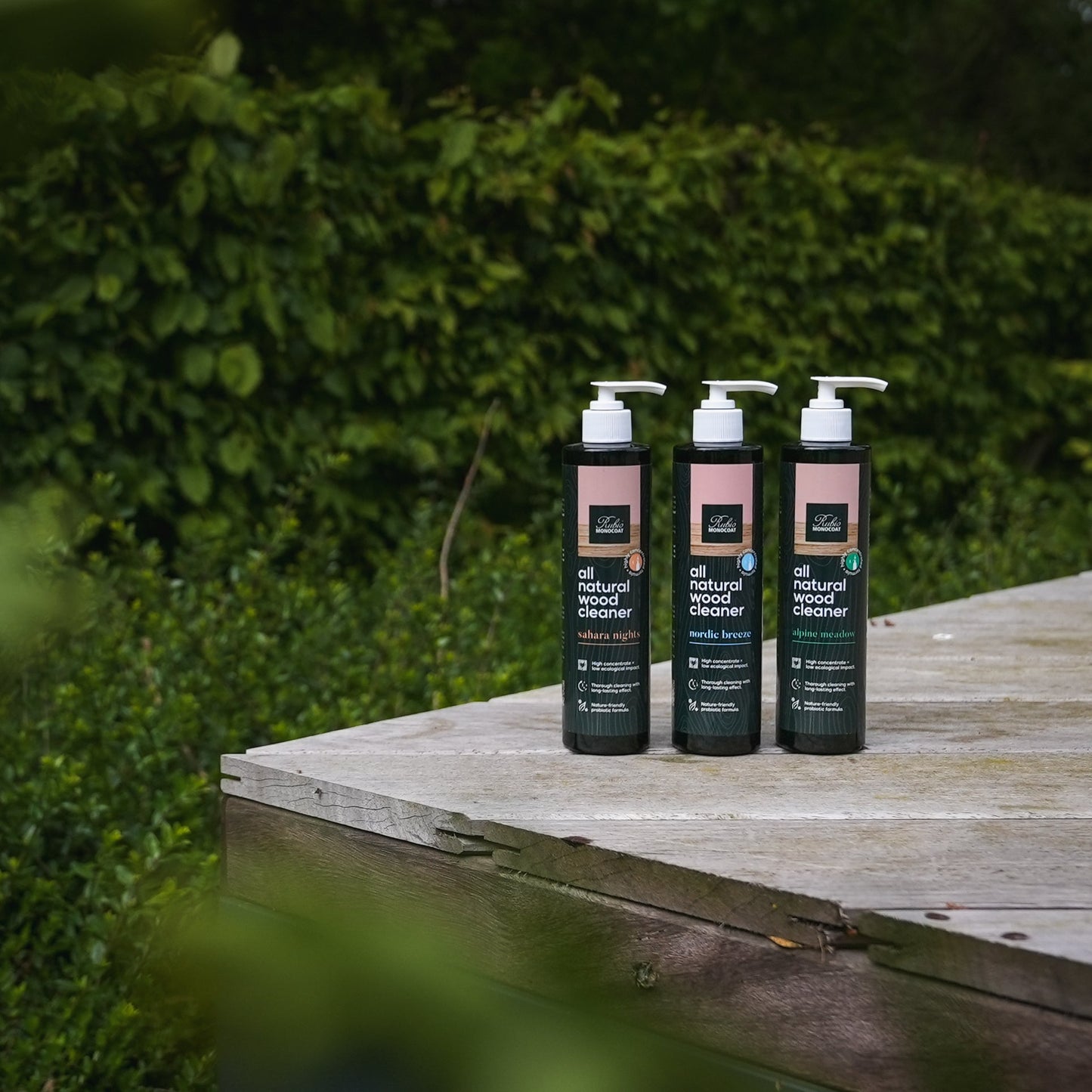 Three bottles of all Natural Wood Cleaner by Rubio Monocoat on a wooden surface.